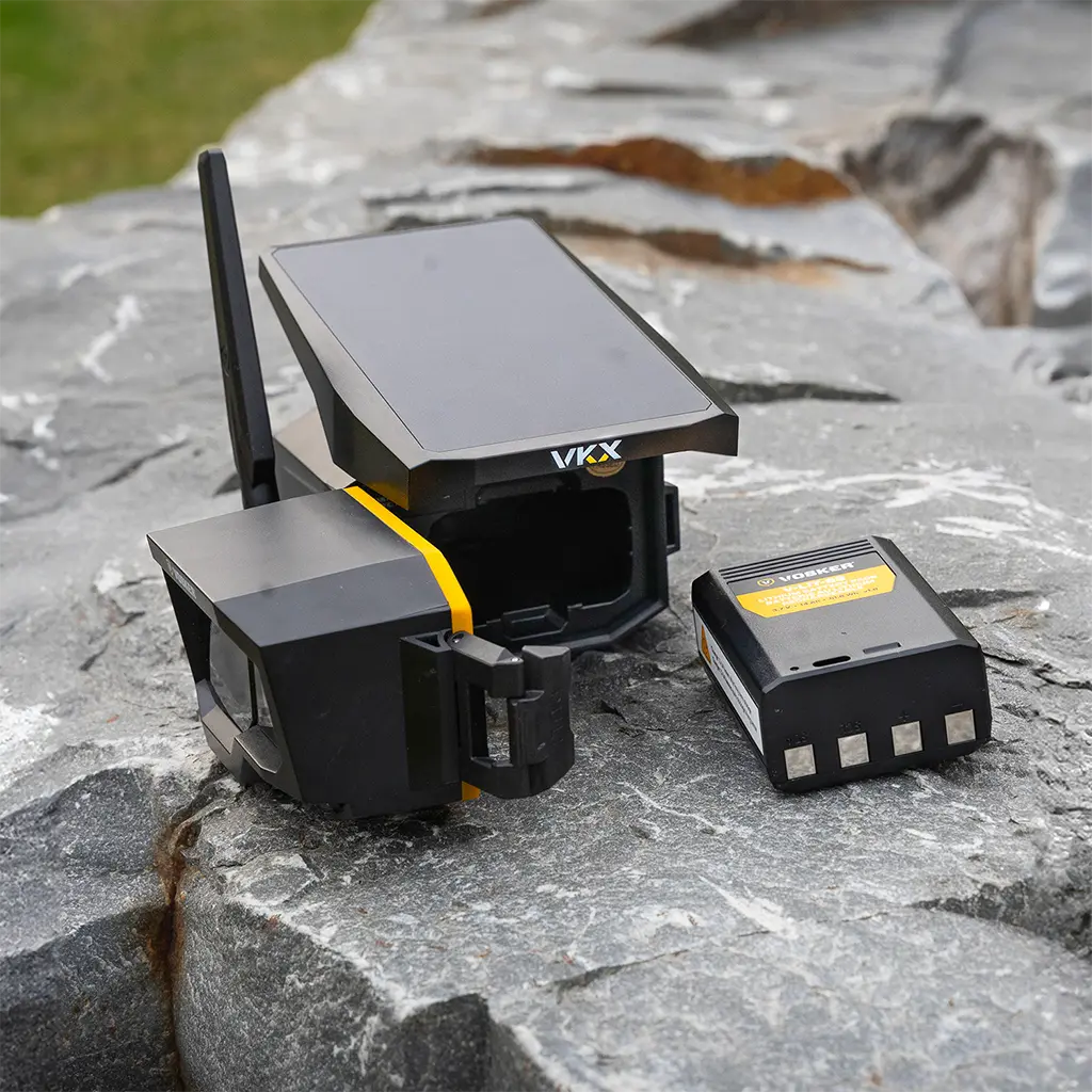Vosker VKX Überwachungskamera mit geöffnetem Akkufach und Akku auf Stein